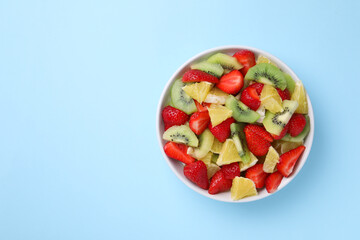 Yummy fruit salad in bowl on light blue background, top view. Space for text