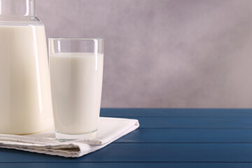 Carafe and glass of fresh milk on blue wooden table, space for text