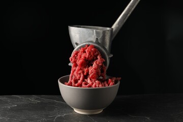 Metal meat grinder with beef mince on dark textured table against black background