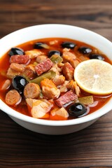 Meat solyanka soup with sausages, olives and vegetables on wooden table, closeup