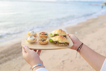 Beachside Dessert Delights: Woman's Hand with Tray of Tarts, Croissants, and Danish