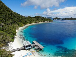 Aerial view of jetty and boats in Wayag Ranger Patrol Post, Raja Ampat, West Papua, Indonesia. Ocean waves, beach and coral reef coastline on tropical island.