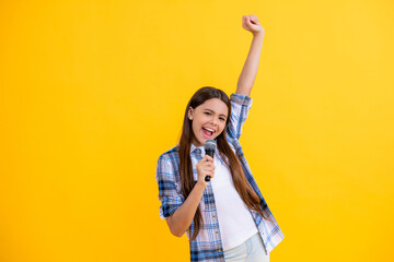 glad teen girl singer hold mic in studio perform karaoke isolated on yellow background