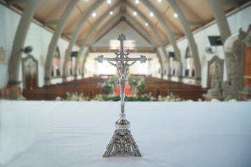 Jesus Christ on cross. Holy cross crucifix stand on the altar with white table and church seats...