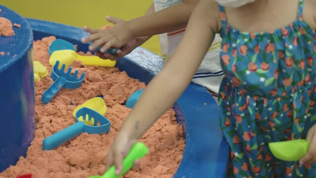 Happy Asian children having fun on entertainment center inflatable castle playing kinetic sand in quarantine, excited girl play sand in sandbox on bounce house attraction playground, Activity playtime