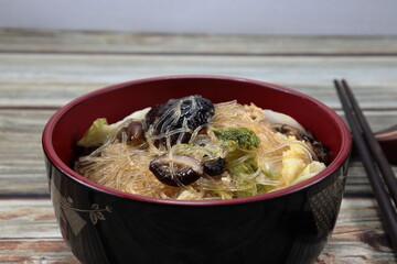Traditional fried and stirred glass noodle mixed with fresh mushroom and cabbage serving in the bowl. Famous vegetarian menu in Asian restaurant.