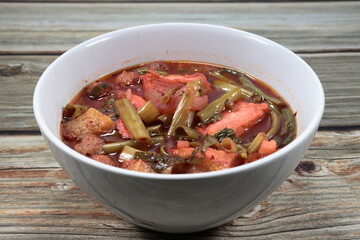 Traditional hot red sauce vegetarian soup mixed with fresh morning glory, plant ball and mushroom serving in the bowl. Famous vegan food in Chinese vegetarian festival.