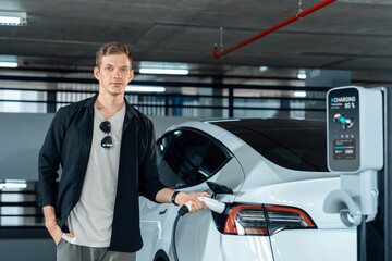 Young man travel with EV electric car to shopping center parking lot charging in downtown city...