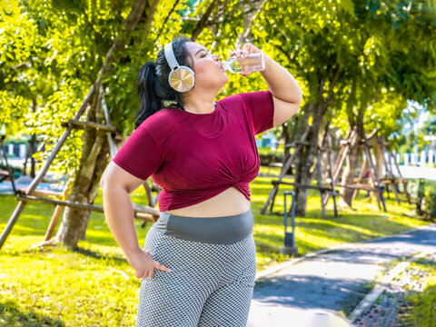 Fat woman wearing sportswear working out and wearing earphones listening to music relaxed breathing fresh air in a green forest  outdoors at the park in the morning with a fresh feeling.