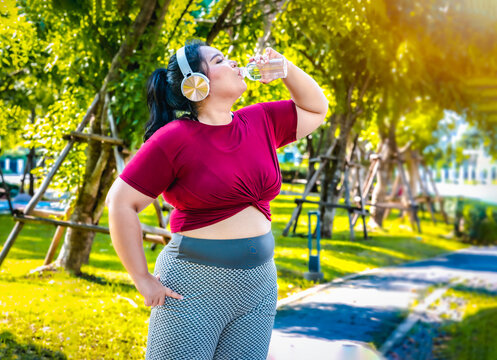 Fat woman wearing sportswear working out and wearing earphones listening to music relaxed breathing fresh air in a green forest  outdoors at the park in the morning with a fresh feeling.