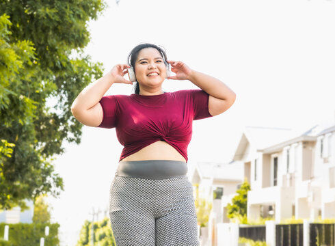 Fat woman wearing sportswear working out and wearing earphones listening to music relaxed breathing fresh air in a green forest  outdoors at the park in the morning with a fresh feeling.
