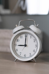 Close-up of a round white alarm clock on a table in the bedroom. The hands on the clock show nine o'clock in the morning, time to get up. Retro alarm clock on the table, vintage tone. space for text