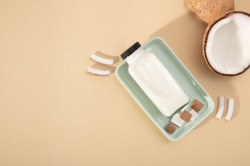 A bottle of coconut milk and chopped fresh coconut are placed on a light green rectangular plate on a pastel background. Minimalist scene for displaying products with coconut ingredients.