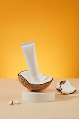 Unlabeled cosmetic tube placed on fresh coconut and white podium, yellow background. Blank space for text design and image insertion. Scene for advertising. Vegan, environmentally friendly cosmetics.