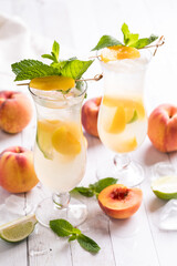 Two peach mojito cocktails surrounded by peaches against a light background.