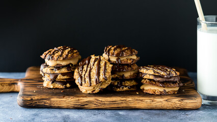 Chocolate and caramel lace cookies on a wooden board with a glass of milk.