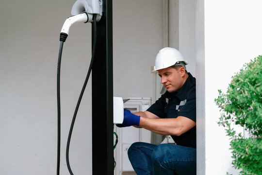 Qualified technician install home EV charging station, providing maintenance service for electric vehicle's battery charging platform at home. EV car technology for residential utilization. Synchronos