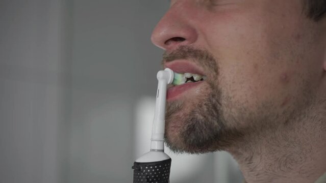 Theme of brushing and whitening teeth with a modern electric toothbrush. Close-up of a man cleaning his teeth with an ultrasonic dental brush. Morning routine, oral hygiene. Oscillating toothbrush. 