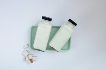 Two bottles of coconut milk placed on a pastel green rectangular plate, adorned with fresh coconut cut into pomegranate-shaped pieces. Coconut milk provides a rich source of electrolytes.