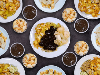 Plates of tahu tek telur with kerupuk or chips and petis sauce on a dark background. Tahu tek is originated from Surabaya, an authentic Indonesian food.