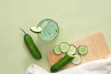 Fresh cucumbers sliced on wooden cutting board, glass of cucumber detox water, towel on pastel background. Cucumber water contains many substances that help purify the body.