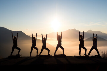 Healthy lifestyle, states of mind concept. Men and women doing yoga or meditation in mountains during sunny and warm summer sunset or sunrise. Dark human silhouettes in foggy mountains background