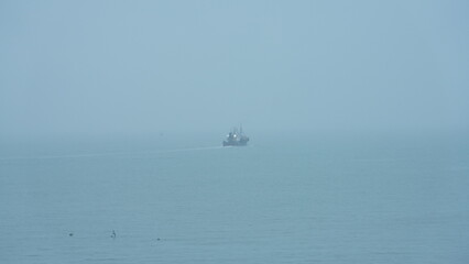 The peaceful sea view with the fishing boat sailing on it in the cloudy day