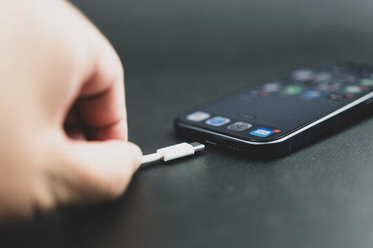 Bangkok, Thailand - October 27, 2023 : Close up of man connects usb type-c cable to iPhone 15 Pro blue Titanium. Type C wired Charger.