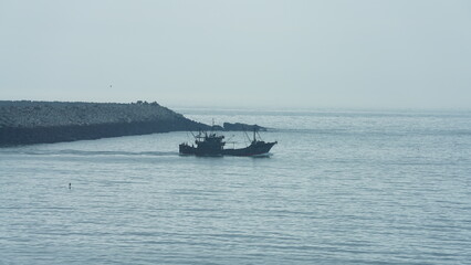 The peaceful sea view with the fishing boat sailing on it in the cloudy day
