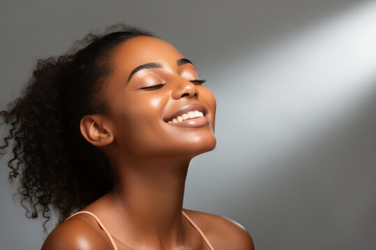 Close-up of a young black woman with her head tilted up with her eyes closed and a smile on her face, on a white background. Chiaroscuro color harmonies. Sincere and natural. Copy space