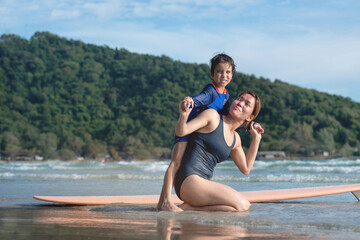Fototapeta na wymiar Mother and son sit and play together on the beach, relaxing after surfing, lifestyle activities, water sports