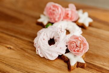 Fototapeta na wymiar Gingerbread cookies in the shape of stars, pink merengue cookies and pink roses on a wooden brown natural table. Christmas and Winter card. Delicious pastries close-up. Valentine’s Day background