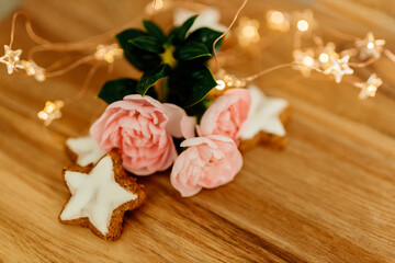 Gingerbread cookies in the shape of stars and pink roses on a wooden table against a background of bokeh of New Year’s lights. Christmas background. Winter card. Delicious pastries