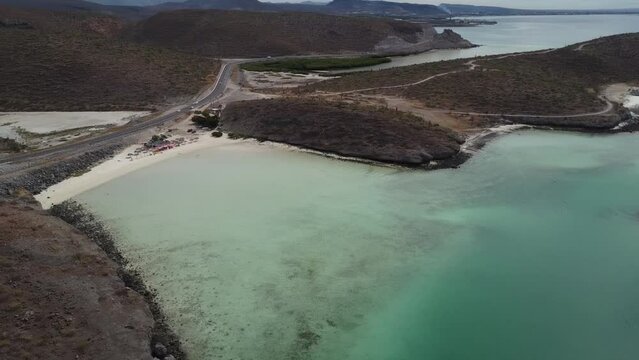 Aerial panorama view in front of the beautiful coast of Playa El Tecolote in Baja California Sur Mexico overlooking the calm sea, dry landscape and a road right on the coast during an adventurous trip