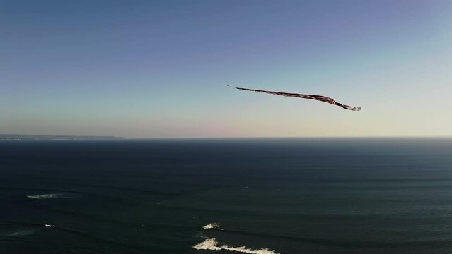 Janggan kite with long tail soaring in sky high above sea in Bali.