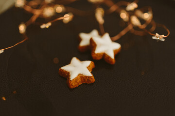 Gingerbread cookies in the shape of stars on a black table against a background of bokeh of New Year's golden lights. Christmas background. Winter card. Delicious pastries close-up
