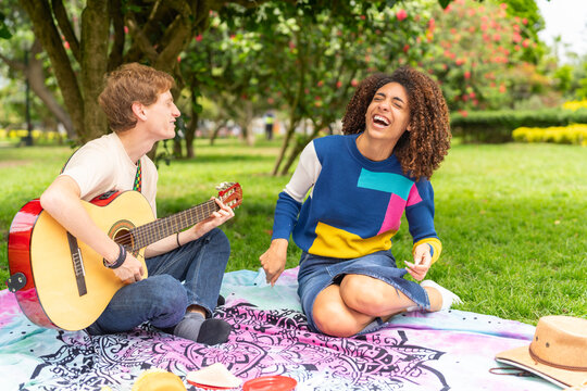 Couple playing guitar and laughing sitting on a picnic blanket