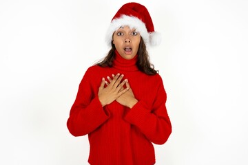 Scared Beautiful woman wearing christmas hat looks with frightened expression, keeps hands on chest, being puzzled to notice something strange, People, hush reaction and emotions.