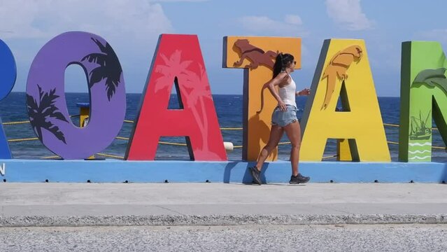 long hair Latina runs slo mo along Roatan sign on island waterfront