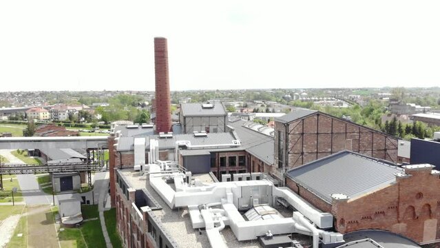 Aerial view of the Żnin Arche Hotel inside old sugar factory in Poland. The tall chimney of the factory is a famous landmark, rising above the surrounding landscape. Descending shot.