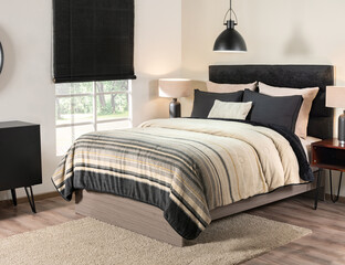 A Nordic-style bedroom with a black upholstered headboard, pillows, a striped quilt in beige and...
