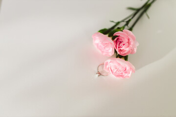 Delicate pink roses and diamond engagement ring on a white backgroundclose up. Pink carnations. Beautiful flowers, a gift for February 14, Valentine's Day, Mother's Day. Place for text. Mock up.