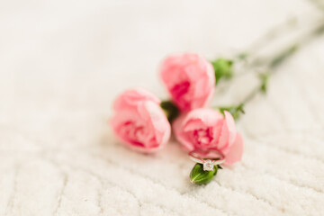 Delicate pink roses and diamond engagement ring on off white fluffy carpet close up. Pink carnations. Beautiful flowers, a gift for February 14, Valentine's Day, Mother's Day. Place for text. Mock up.