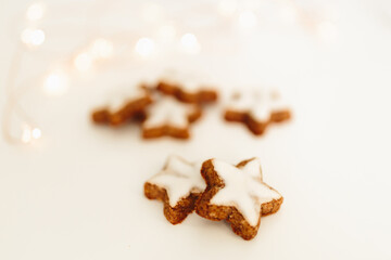 Gingerbread cookies in the shape of stars on a white table against a background of bokeh of New Year's golden lights. Christmas background. Winter card. Delicious pastries close-up