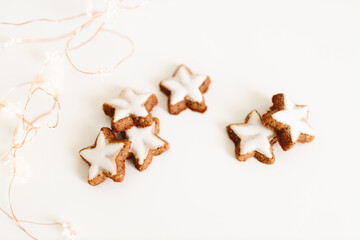 Fototapeta na wymiar Gingerbread cookies in the shape of stars on a white table against a background of bokeh of New Year's golden lights. Christmas background. Winter card. Delicious pastries close-up