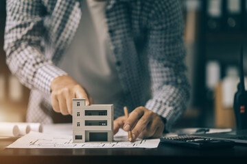 Fototapeta premium Close up of male architect hands making model house. Man architect working in the office.
