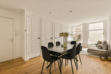 a dining table and chairs in a living room with white walls, hardwood flooring and large windows looking out onto the street