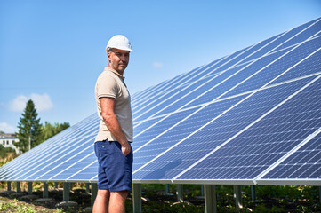 Professional worker checking PV solar panels. Adult man standing next to modern energy resource....