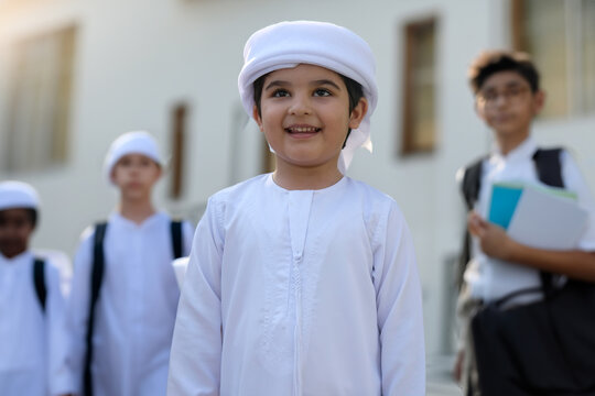 Happy Arab Middle Eastern boy wearing traditional white kandura smiling with classmates in a modern classroom setting. Young Emirati schoolboy enjoying school day with schoolmates for primary educatio
