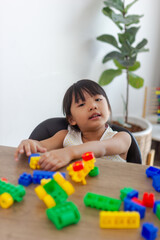 Fototapeta na wymiar Cute funny preschooler little girl in a colorful shirt playing with construction toy blocks building a tower in a sunny kindergarten room. Kids playing. Children at day care. Child and toys.